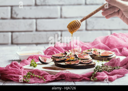Pane fresco con fichi, ricotta e miele bianco sul bordo di taglio Foto Stock