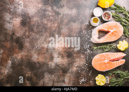 Crudo fresco bistecca di salmone, limone, rosmarino e spezie on dark rustico sfondo concreto. Telaio alimentare vista superiore con copia spazio. Impostare gli ingredienti per la realizzazione di Foto Stock