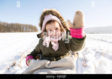 Carino bambina fuori in inverno la natura, seduto sulla slitta Foto Stock