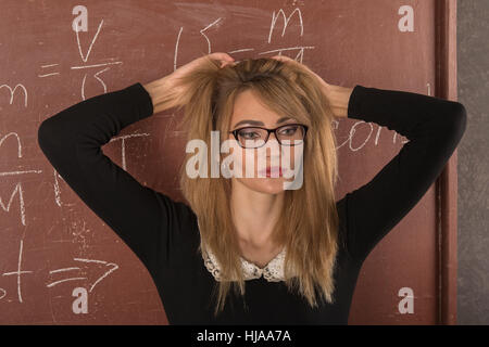 Affascinante ragazza in abito nero vicino alla lavagna. Foto Stock