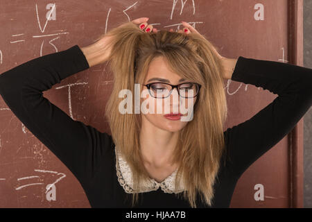 Affascinante ragazza in abito nero vicino alla lavagna. Foto Stock