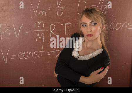 Affascinante ragazza in abito nero vicino alla lavagna. Foto Stock