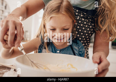 Bellissima bambina con sua madre pastella di miscelazione in un recipiente e sorridente. Madre e figlia in cucina la preparazione della pastella per la cottura. Foto Stock
