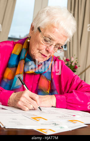 Una vecchia signora organizzando la sua spesa mensile in casa sua nel tentativo di risparmiare denaro Foto Stock