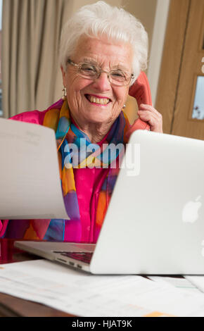 Una vecchia signora organizzando la sua spesa mensile in casa sua nel tentativo di risparmiare denaro Foto Stock