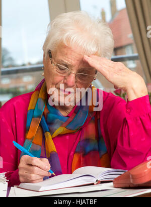 Una vecchia signora organizzando la sua spesa mensile in casa sua nel tentativo di risparmiare denaro Foto Stock