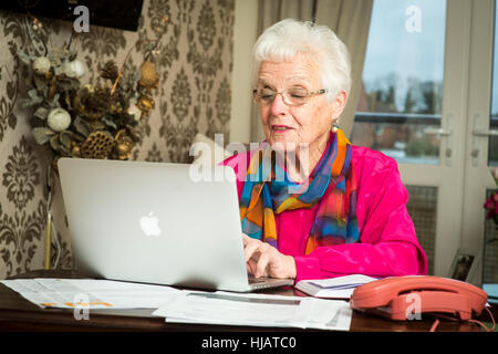 Una vecchia signora organizzando la sua spesa mensile in casa sua nel tentativo di risparmiare denaro Foto Stock