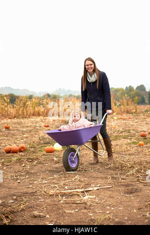 Ritratto di metà donna adulta spingendo il toddler figlia in carriola in campo di zucca Foto Stock