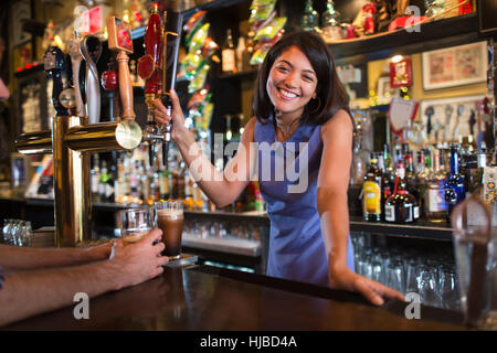 Ritratto di giovane donna barista che serve birra in casa pubblica Foto Stock