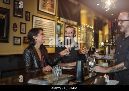 Barista e coppia giovane elevare un toast in public house Foto Stock