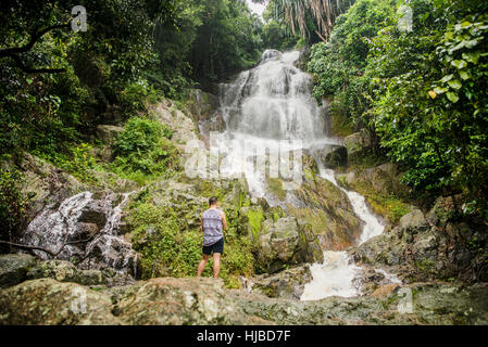 Giovane uomo in piedi sulla roccia a guardare Na Muang cascata, Koh Samui, Thailandia Foto Stock