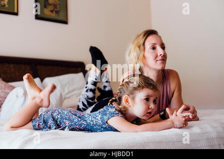 Donna sdraiata sul letto con il toddler figlia guardi la TV Foto Stock