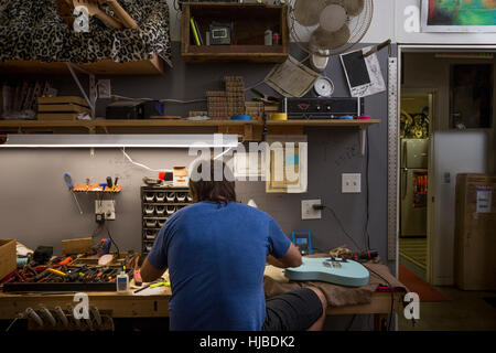 Vista posteriore del liutaio seduto alla scrivania di chitarra di fabbricazione Foto Stock