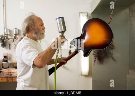 Liutaio in officina con la pistola a spruzzo per verniciatura di chitarra Foto Stock