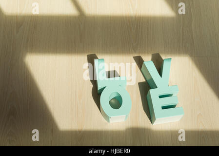 Legno verde lettere che compongono la parola amore mettendo su sfondo di legno. Foto Stock