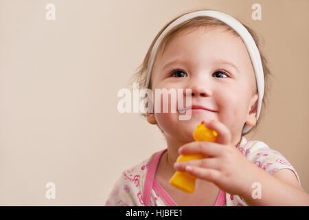 Baby ragazza sorridente Holding Toy guardando la fotocamera Foto Stock