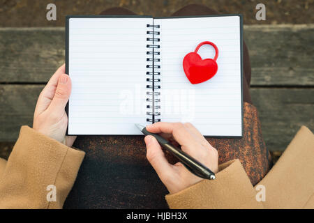 Mani femminili azienda notebook chiuso con lucchetto rosso a forma di cuore e matita Foto Stock