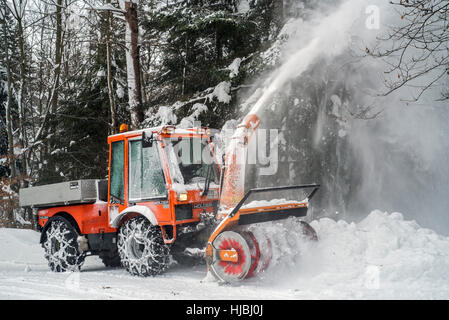 Titolare C9700H trattore comunale con lo spalaneve sgombero della neve dalla strada nella foresta dopo la nevicata in inverno Foto Stock