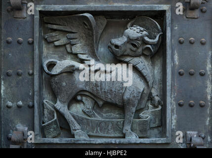 Toro alato di San Luca. Dettaglio del portone di bronzo alla Basilica de la Santa Cruz (Basilica di Santa Croce) nella Valle de los Caidos (Valle dei Caduti) vicino a Madrid, Spagna. Foto Stock