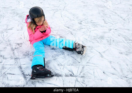 Bambino ragazza seduta sul ghiaccio dopo la caduta nel parco innevato durante le vacanze invernali Foto Stock