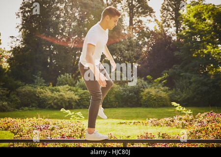 Uomo di formazione, in equilibrio su una gamba sul recinto del parco Foto Stock