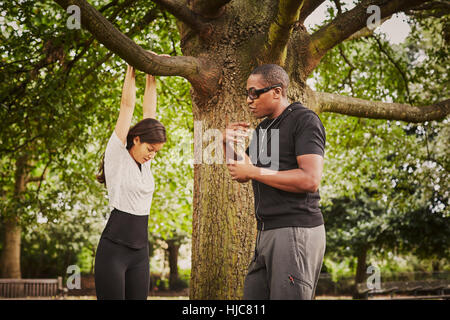 Personal trainer istruire la donna su pull ups tramite park ramo di albero Foto Stock