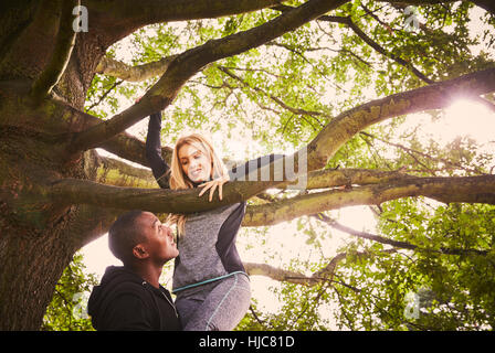 Personal trainer sollevamento di giovane donna a salire park tree Foto Stock