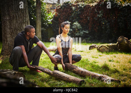 Donna con personal trainer accovacciato per sollevare il tronco di albero in posizione di parcheggio Foto Stock