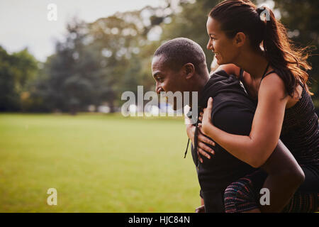 Uomo e donna con formazione di divertimento nel parco, dando piggy back Foto Stock