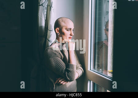 Ritratto di giovane donna con la testa rasata guardando attraverso la finestra Foto Stock