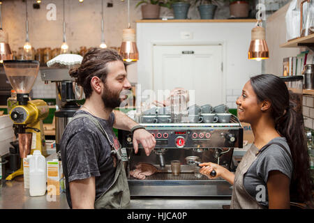 Maschio e femmina baristi parlando da caffè con macchina per il caffè Foto Stock