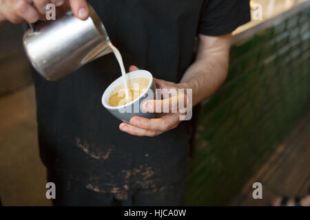 Barista maschio con le mani in mano versando il latte nella tazza di caffè nella caffetteria Foto Stock