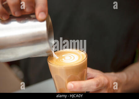 Chiusura del barista le mani versando il latte nel caffè nella caffetteria Foto Stock