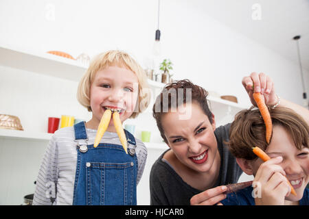 Giovane donna, un ragazzo e una ragazza in cucina, ingannare intorno, utilizzando le carote come denti finti Foto Stock