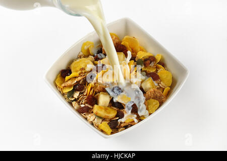 Versare il latte in un recipiente di corn flakes e cereali su sfondo bianco - close up Foto Stock