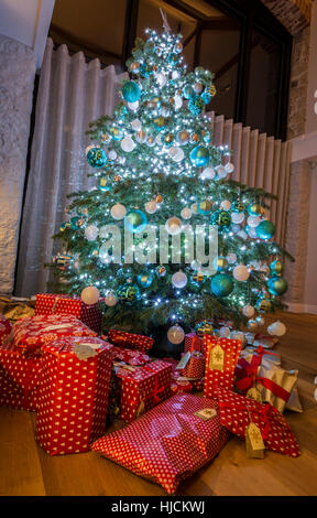 Grande albero di Natale con doni avvolto/presenta in casa in Inghilterra UK.tree ha le luci di Natale e baubles.Gli scaffali in B/G Foto Stock