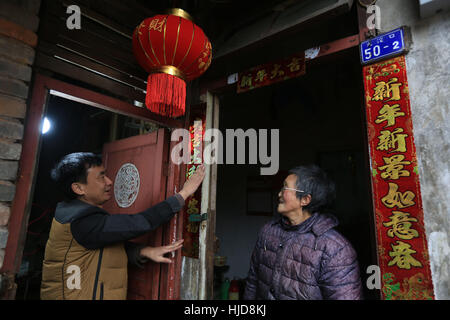 Chongqing Cina. 23 gen 2017. Un volontario (L) paste Festival di Primavera baciata sulla porta di Liu Huiying della casa di Chongqing, a sud-ovest della Cina, 23 gennaio, 2017. Volontari su lunedì ha visitato Liu Huiying, una donna anziana che vive da sola e aveva una riunione di famiglia pasto con lei in tempo per il Festival di Primavera. Credito: Qin Tingfu/Xinhua/Alamy Live News Foto Stock