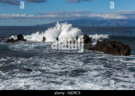 Onde che si infrangono sulle rocce della costa occidentale di Tenerife con l'isola di La Gomera in background. Isole Canarie Spagna Foto Stock
