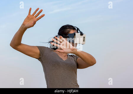 Donna (in 40s) indossando una realtà virtuale auricolare (VR) di maschera e guarda come protetto se stessa Foto Stock