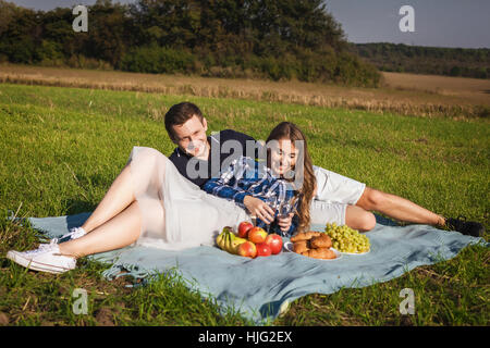 Giovane coppia felice al picnic sull'erba verde con banane, mele, vino e uva Foto Stock