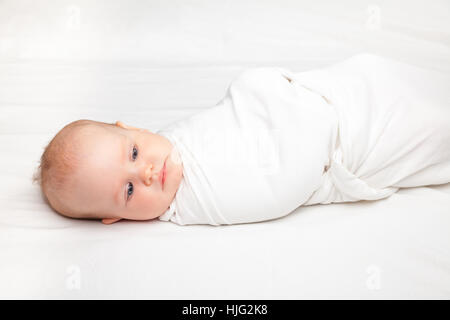 Tre mese Baby girl avvolto in un moderno baby alato swaddle posa su un  letto. La