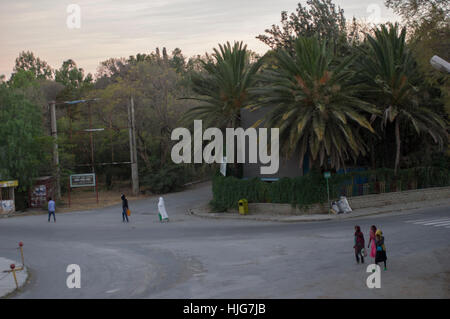 Street a Nord dell'Etiopia, Mekelle con persone in vesti bianche e abbigliamento quotidiano passando le palme Foto Stock