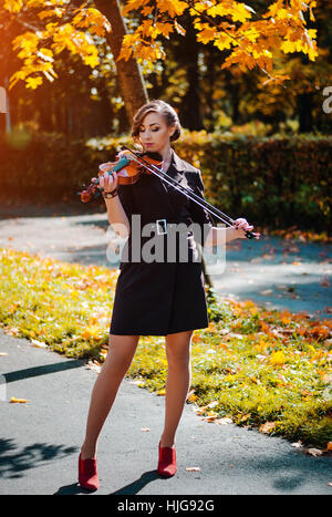 Ritratto di ragazza intelligente con violino sulle mani per esterno in cappotto marrone in autunno. Foto Stock