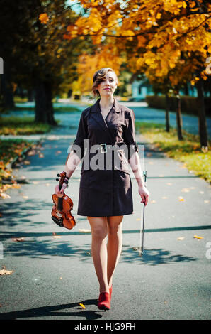 Ritratto di ragazza intelligente con violino sulle mani per esterno in cappotto marrone in autunno. Foto Stock