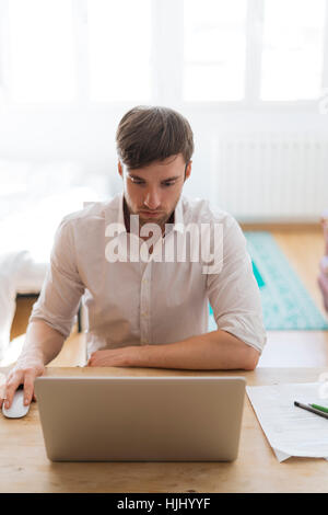 Giovane uomo che lavora da casa con il computer portatile Foto Stock