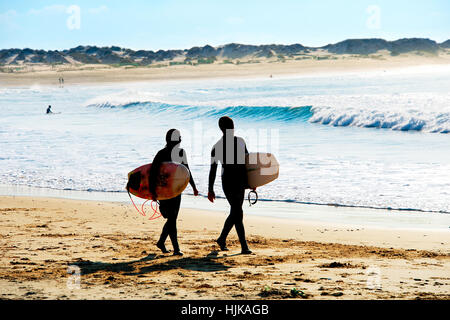 Surfers giovane camminando sulla spiaggia dell'oceano Foto Stock