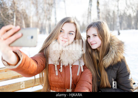 Due ragazze sorridenti rendere selfie in winter park Foto Stock