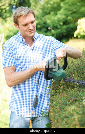 Uomo taglio siepe Giardino con rifinitore elettrico Foto Stock