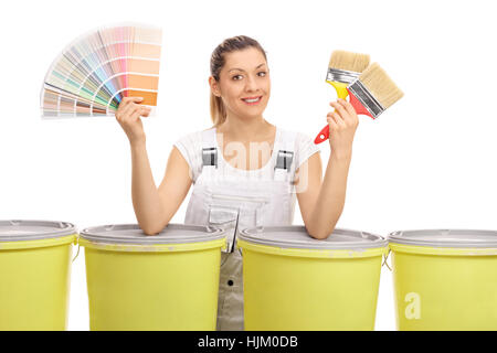 Allegro pittore femmina con un campione di colore e pennelli dietro le benne di colore isolato su sfondo bianco Foto Stock