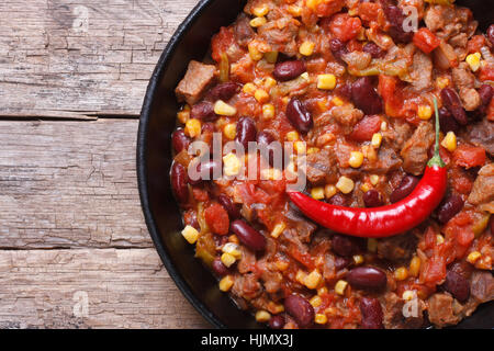 Chili con carne di close-up in una padella su un sfondo di legno. orizzontale vista superiore Foto Stock